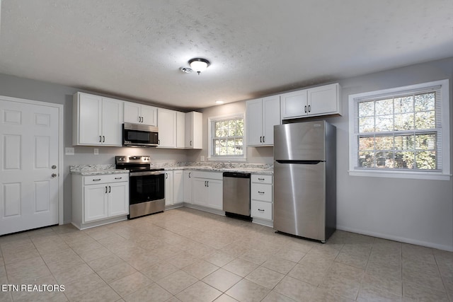 kitchen featuring stainless steel appliances, light tile patterned floors, plenty of natural light, and white cabinets