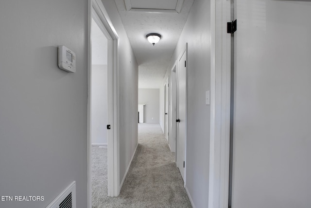 hallway featuring a textured ceiling and light colored carpet