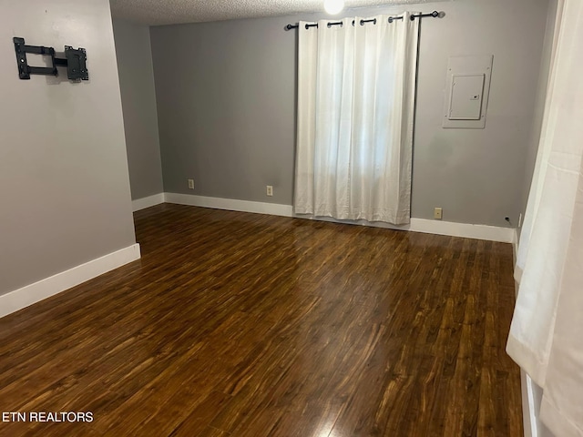 spare room with a textured ceiling, electric panel, and dark hardwood / wood-style floors