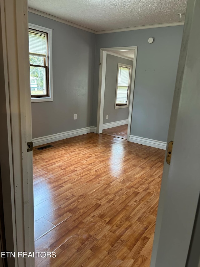 empty room featuring light hardwood / wood-style floors, a textured ceiling, and ornamental molding