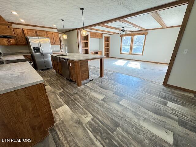 kitchen with hanging light fixtures, appliances with stainless steel finishes, a textured ceiling, a kitchen island with sink, and dark wood-type flooring