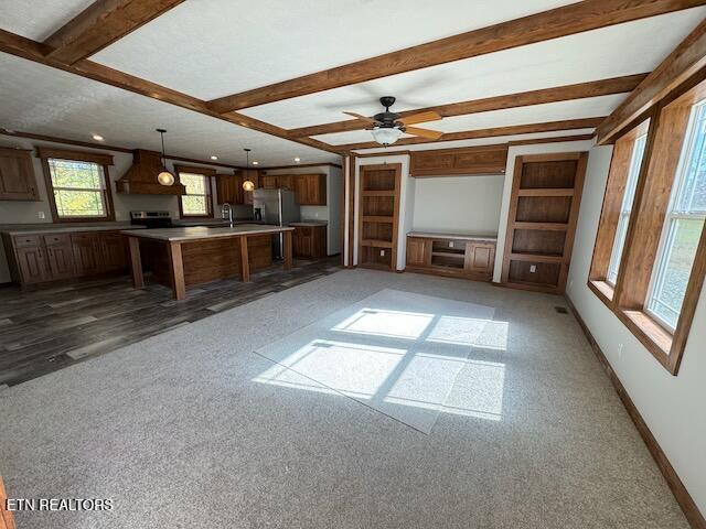 unfurnished living room featuring sink, ceiling fan, beam ceiling, and dark carpet