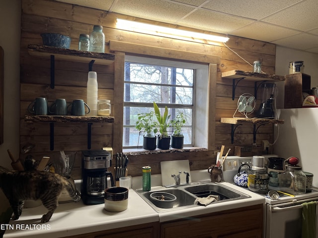 kitchen featuring a drop ceiling, sink, wood walls, and white range with electric cooktop