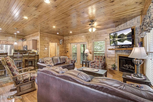 living room featuring a stone fireplace, wood ceiling, a ceiling fan, and wooden walls