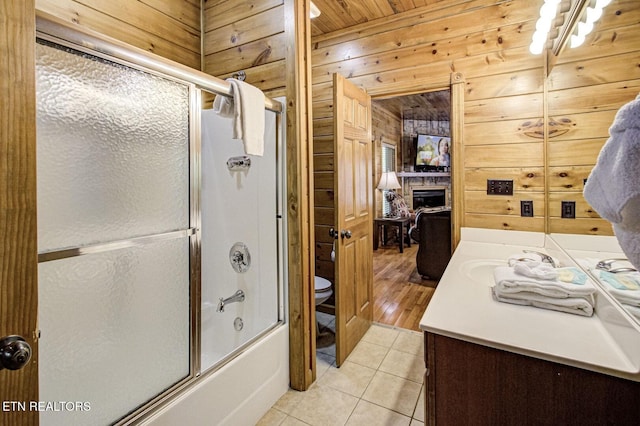 bathroom with bath / shower combo with glass door, toilet, tile patterned floors, wood walls, and vanity