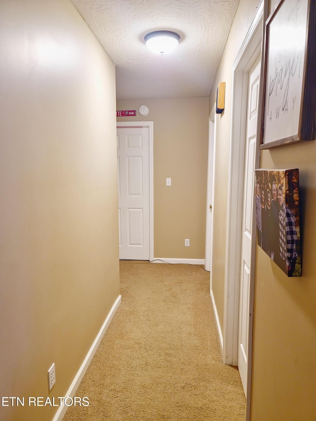 hallway with a textured ceiling and light carpet