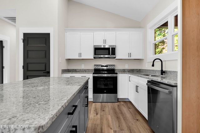 kitchen with vaulted ceiling, stainless steel appliances, sink, and white cabinets