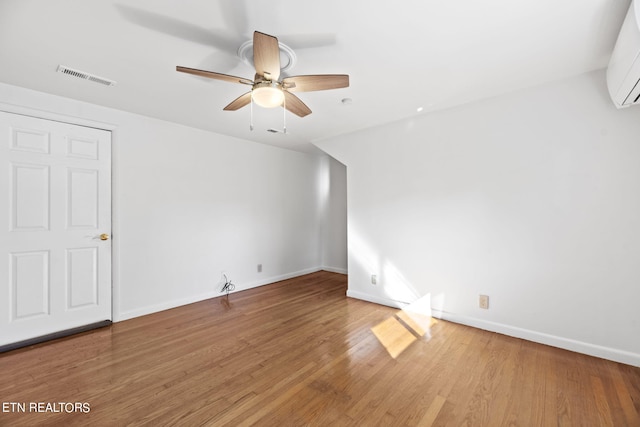 spare room with a wall unit AC, hardwood / wood-style flooring, and ceiling fan