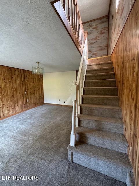 stairway with a textured ceiling, carpet flooring, wood walls, and a notable chandelier