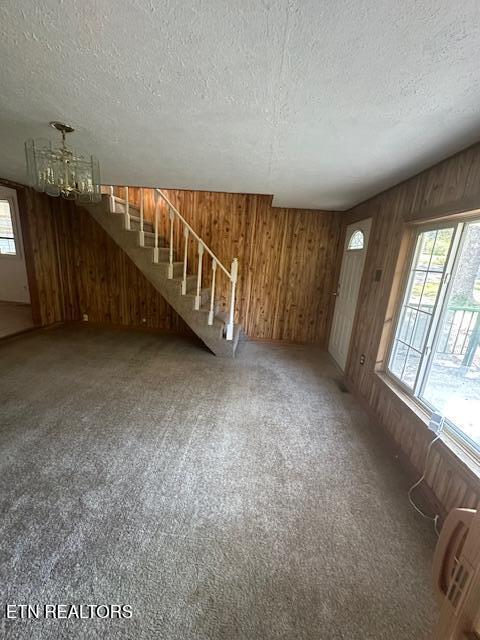 unfurnished living room featuring a textured ceiling, a chandelier, carpet flooring, and wood walls