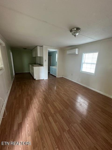 unfurnished living room with a wall mounted AC, dark wood-type flooring, and sink