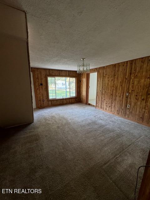 spare room featuring a textured ceiling, an inviting chandelier, carpet, and wooden walls