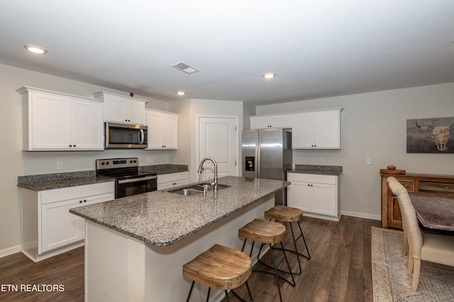 kitchen featuring a center island with sink, appliances with stainless steel finishes, white cabinetry, dark wood-type flooring, and sink