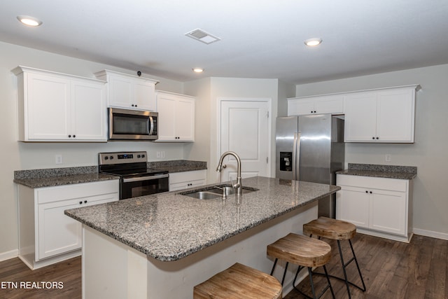 kitchen with dark wood-type flooring, a center island with sink, sink, white cabinetry, and appliances with stainless steel finishes