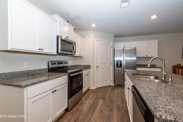 kitchen featuring stainless steel appliances, a sink, white cabinetry, dark wood-style floors, and dark stone countertops