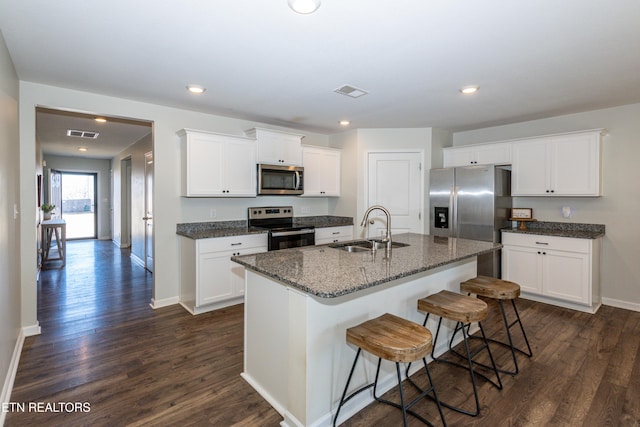 kitchen with a kitchen island with sink, stainless steel appliances, a sink, and white cabinetry