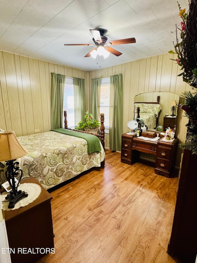 bedroom with wooden walls, light wood-type flooring, and ceiling fan