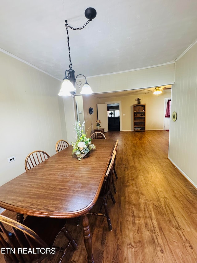 dining space featuring crown molding, wood-type flooring, wooden walls, and ceiling fan with notable chandelier