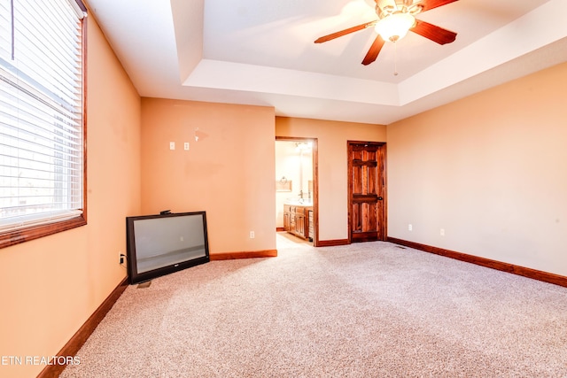 carpeted spare room with a raised ceiling and ceiling fan