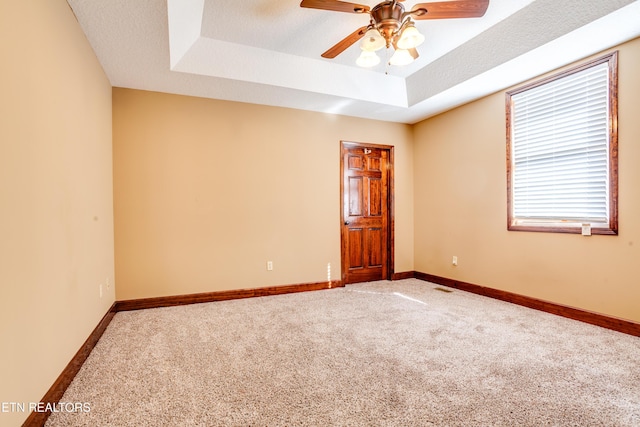 empty room featuring ceiling fan, carpet flooring, and a tray ceiling