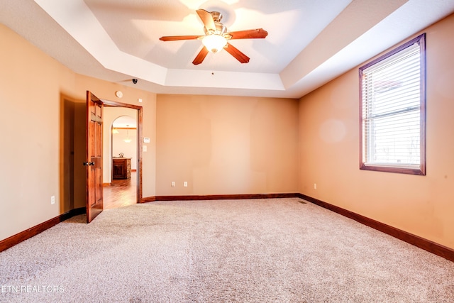 carpeted spare room featuring ceiling fan and a raised ceiling