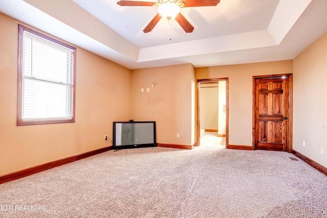 carpeted spare room with ceiling fan and a tray ceiling