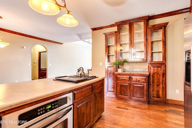 kitchen featuring crown molding, a textured ceiling, pendant lighting, stainless steel appliances, and light hardwood / wood-style floors