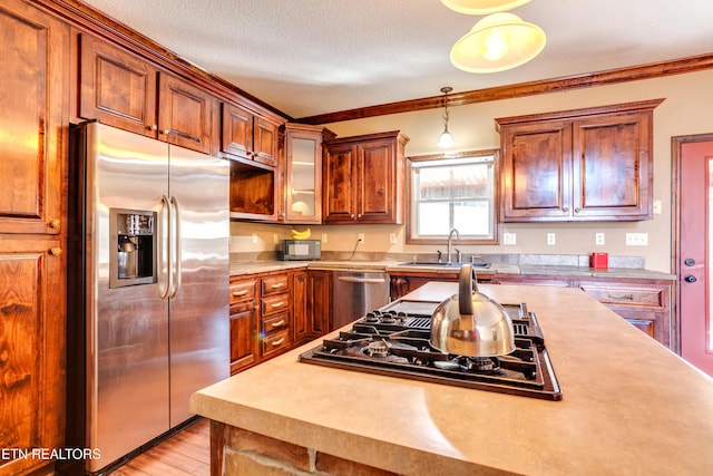 kitchen with sink, hanging light fixtures, stainless steel appliances, crown molding, and a textured ceiling