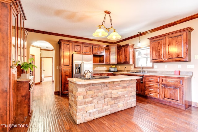 kitchen with sink, stainless steel fridge with ice dispenser, hanging light fixtures, ornamental molding, and a kitchen island