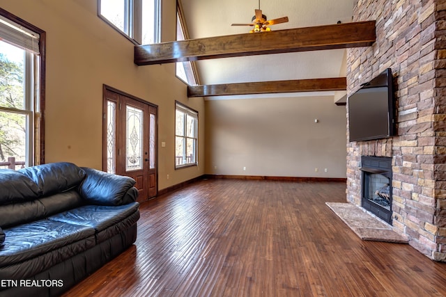 unfurnished living room featuring dark hardwood / wood-style flooring, beamed ceiling, ceiling fan, a fireplace, and a high ceiling