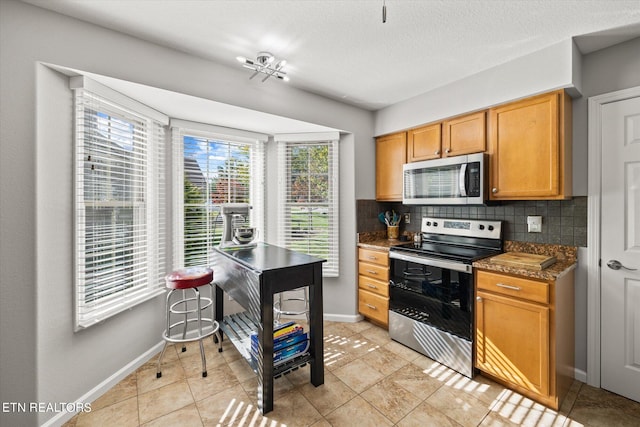 kitchen with light tile patterned floors, appliances with stainless steel finishes, backsplash, a textured ceiling, and dark stone countertops