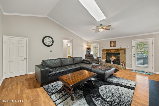 living room with a stone fireplace, ceiling fan, lofted ceiling with skylight, hardwood / wood-style flooring, and ornamental molding