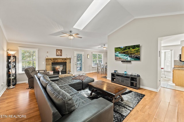 living room with ceiling fan, a healthy amount of sunlight, vaulted ceiling with skylight, and light hardwood / wood-style flooring