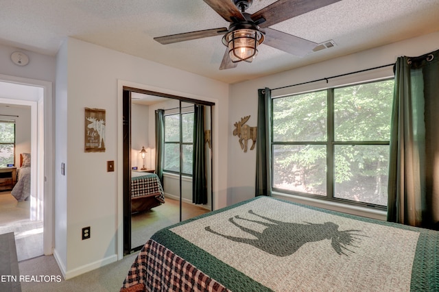 carpeted bedroom with a textured ceiling, multiple windows, a closet, and ceiling fan