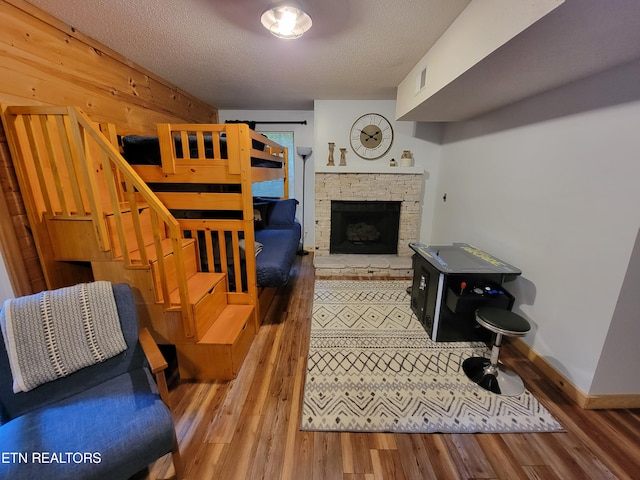 living room featuring a stone fireplace, a textured ceiling, and hardwood / wood-style floors