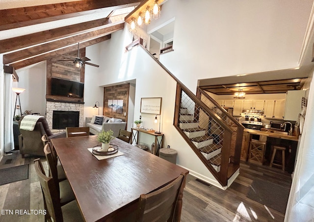 dining area with a stone fireplace, ceiling fan, beamed ceiling, high vaulted ceiling, and dark hardwood / wood-style floors