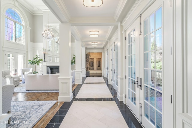 hallway featuring french doors, decorative columns, ornamental molding, and an inviting chandelier