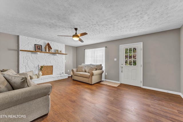 living room with ceiling fan, a textured ceiling, dark hardwood / wood-style flooring, and a fireplace