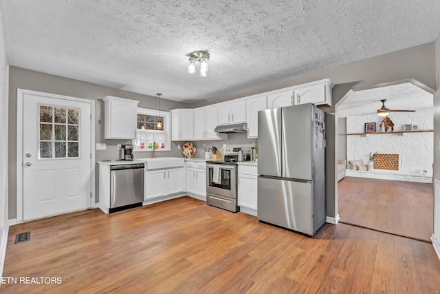 kitchen featuring appliances with stainless steel finishes, hanging light fixtures, light hardwood / wood-style flooring, and white cabinetry