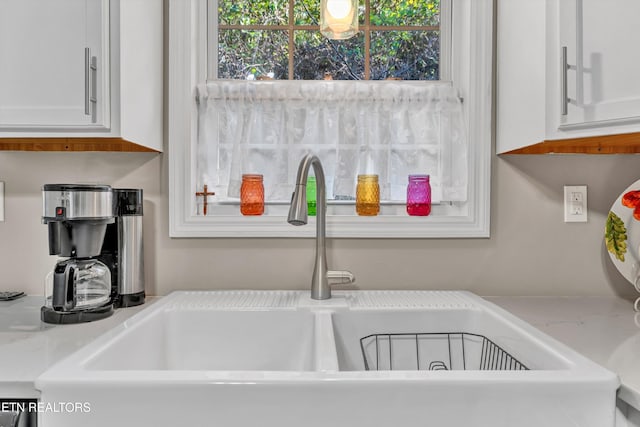 interior details with white cabinetry, sink, and light stone counters