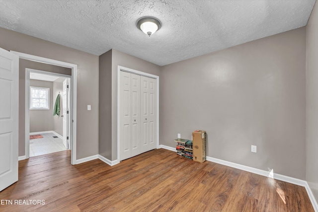 unfurnished bedroom with a textured ceiling, wood-type flooring, and a closet