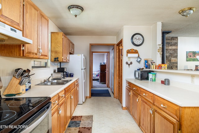 kitchen featuring a wood stove, sink, white refrigerator, a textured ceiling, and stainless steel electric range oven