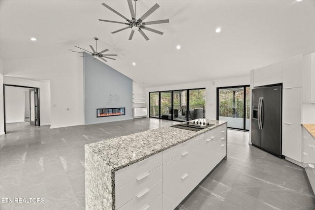 kitchen featuring stainless steel refrigerator with ice dispenser, black electric stovetop, light stone counters, high vaulted ceiling, and white cabinets