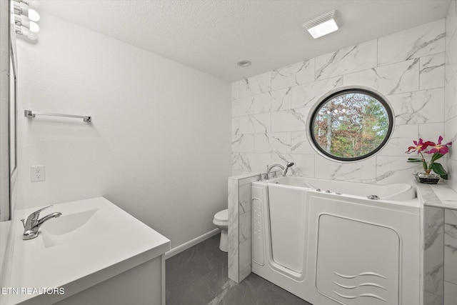 bathroom with a tub to relax in, vanity, a textured ceiling, and toilet