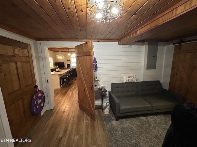 living room with wooden walls, wood-type flooring, wooden ceiling, and a barn door