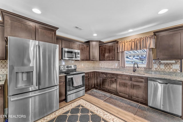 kitchen featuring appliances with stainless steel finishes, light stone countertops, ornamental molding, dark brown cabinetry, and sink