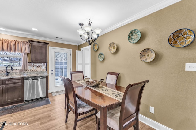 dining room with sink, ornamental molding, light hardwood / wood-style floors, and a notable chandelier