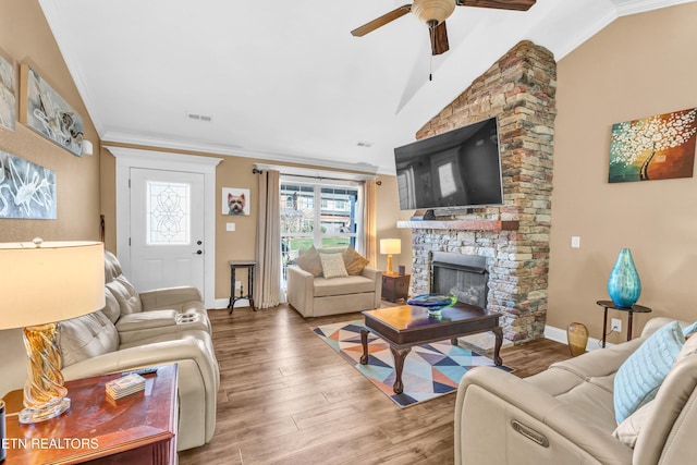 living room featuring vaulted ceiling, wood-type flooring, ornamental molding, ceiling fan, and a fireplace