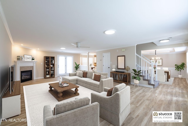 living room with ornamental molding, ceiling fan with notable chandelier, light hardwood / wood-style floors, and a tile fireplace