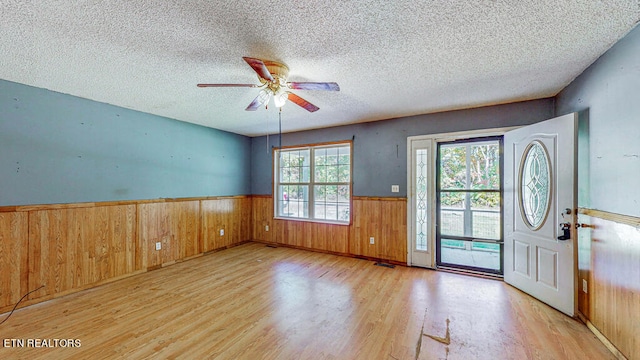 entryway featuring ceiling fan, wood walls, a textured ceiling, and light hardwood / wood-style flooring